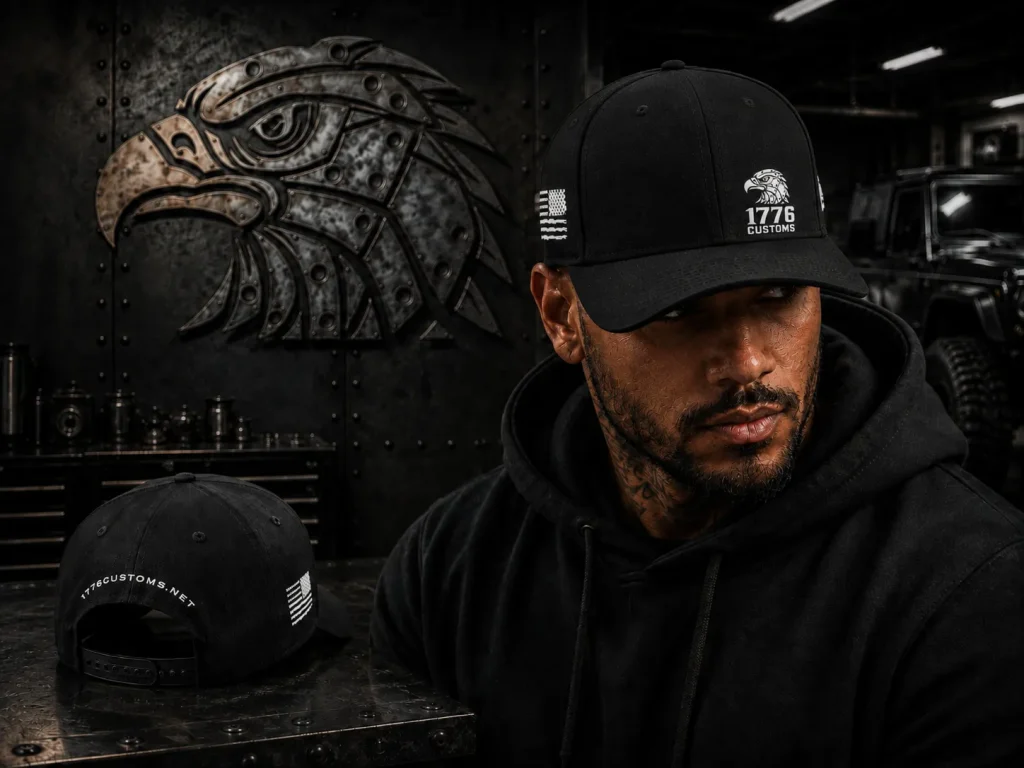 Male model wearing a black 1776 Customs New Era fitted cap with an embroidered eagle logo on the front and an American flag patch on the side, displayed alongside a rear view showing 1776CUSTOMS.NET embroidered on the back.