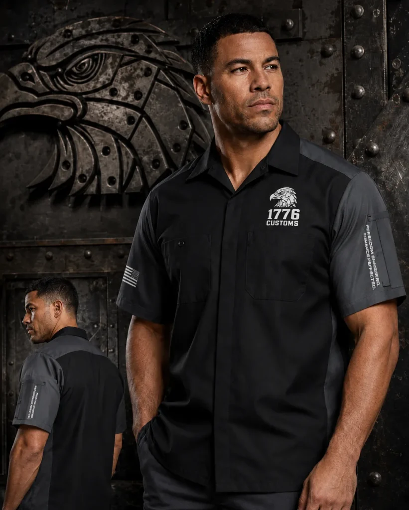 Front and back view of a male model wearing a two-tone black and dark grey short-sleeve shop work shirt by 1776 Customs, featuring dual chest pockets, a white eagle emblem, and a sleeve American flag patch.