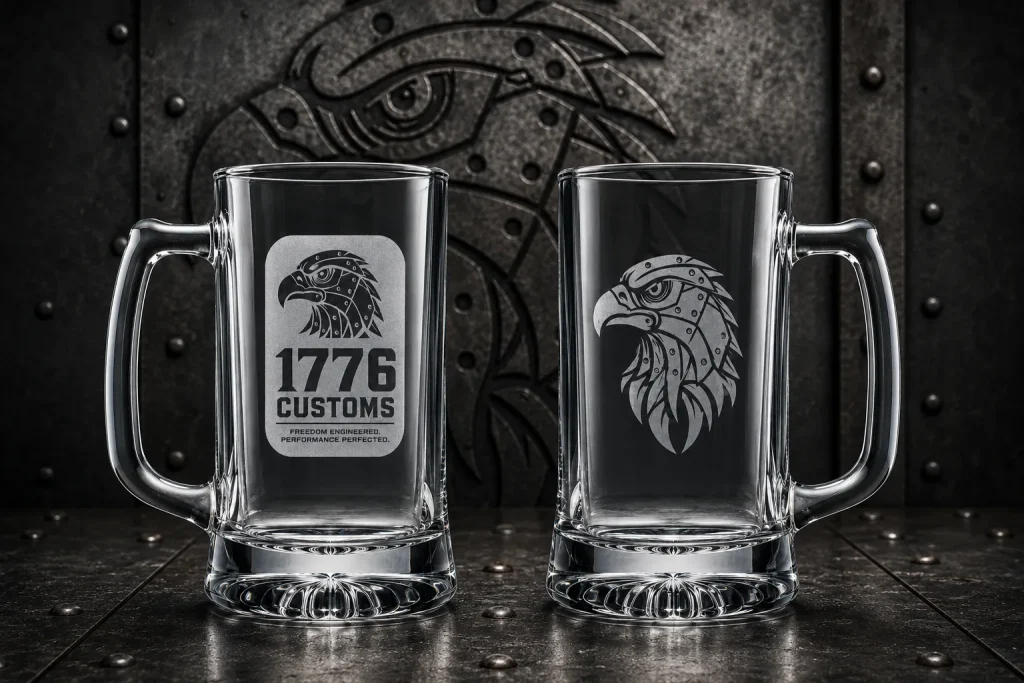 Two etched clear glass beer mugs with 1776 Customs eagle logos on a metallic surface.