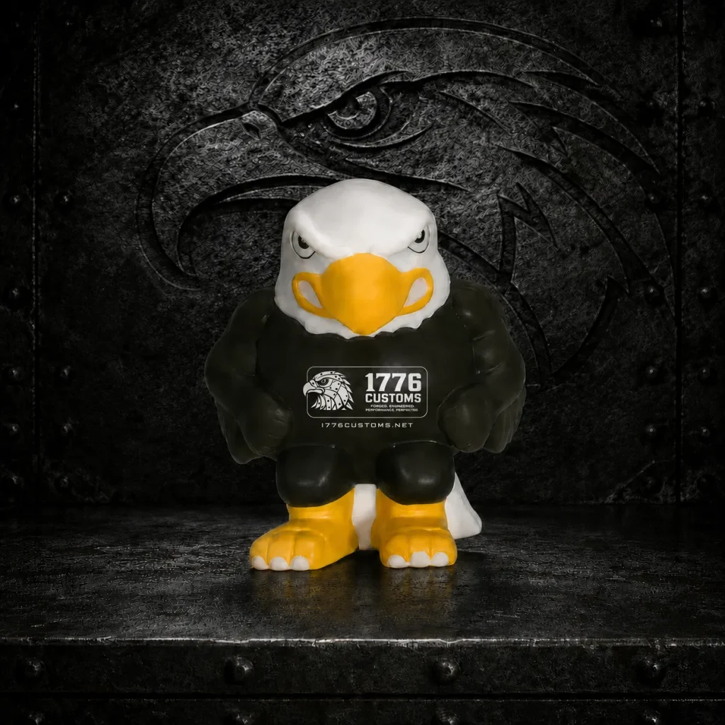 1776 Customs bald eagle foam stress reliever toy with printed logo and website URL on a dark metal background.
